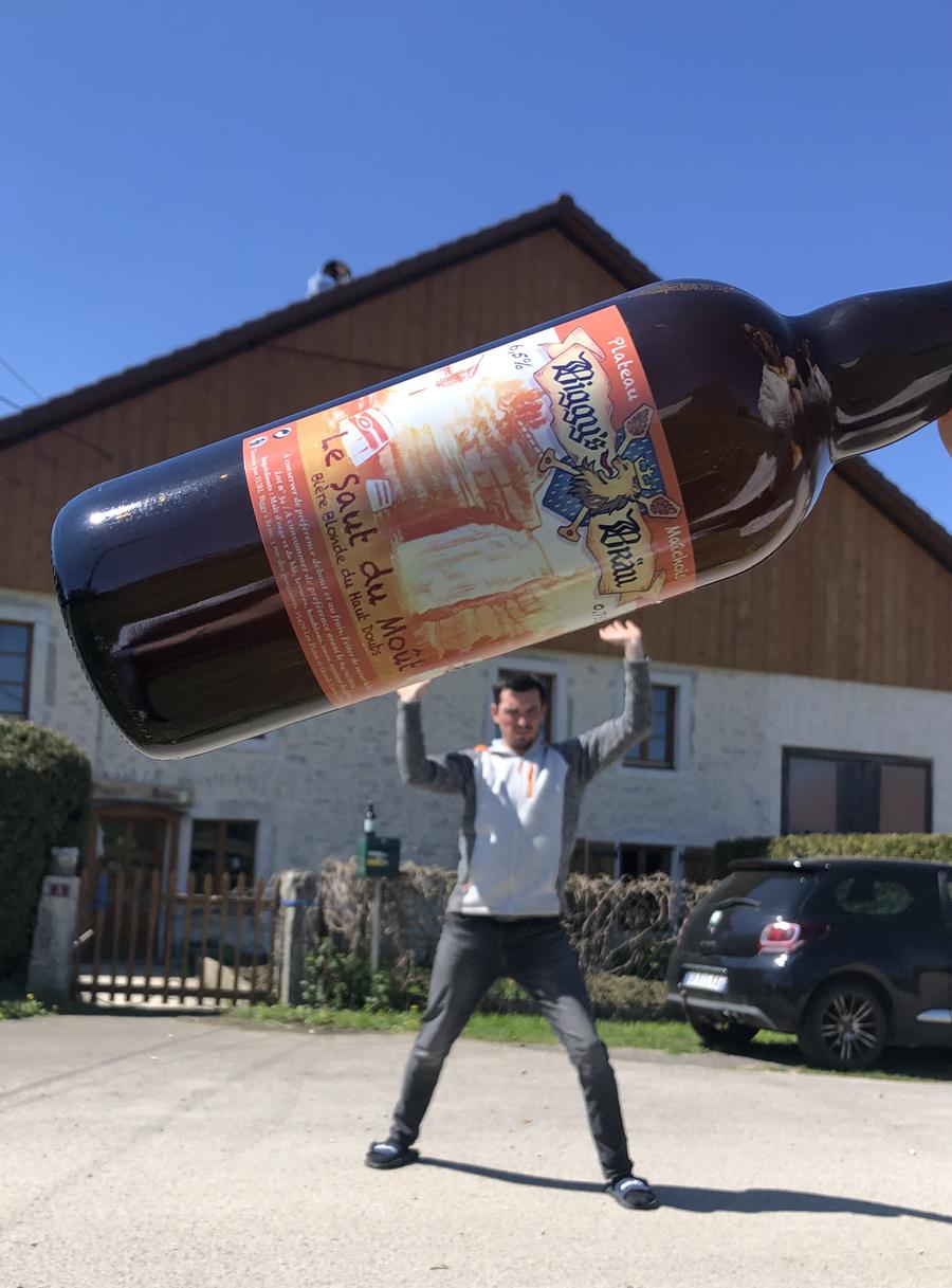 Photo truquée : une bouteille Biggy's Bräu géante portée à bout de bras devant la brasserie